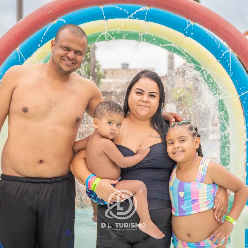 Família posando em frente a um arco colorido com jatos de água.